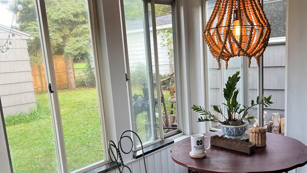 A sunroom with large windows, a round table, and a hanging light fixture.