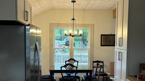 A modern kitchen with a stainless steel refrigerator, wooden cabinets, a dining table with chairs, and a large window with a view of the outdoors.