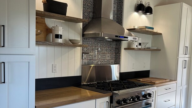 A modern kitchen with white cabinetry, a stainless steel range hood, and a wood-burning stove.