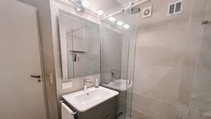 A modern bathroom with a glass shower enclosure, a large mirror, and a white sink.