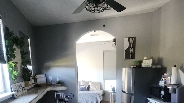 A compact kitchen with a ceiling fan, a refrigerator, a bar stool, and a small dining area.