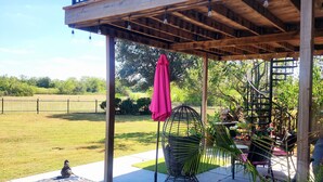 A covered outdoor seating area with a wooden deck, a metal chair, a pink umbrella, and a decorative birdcage.