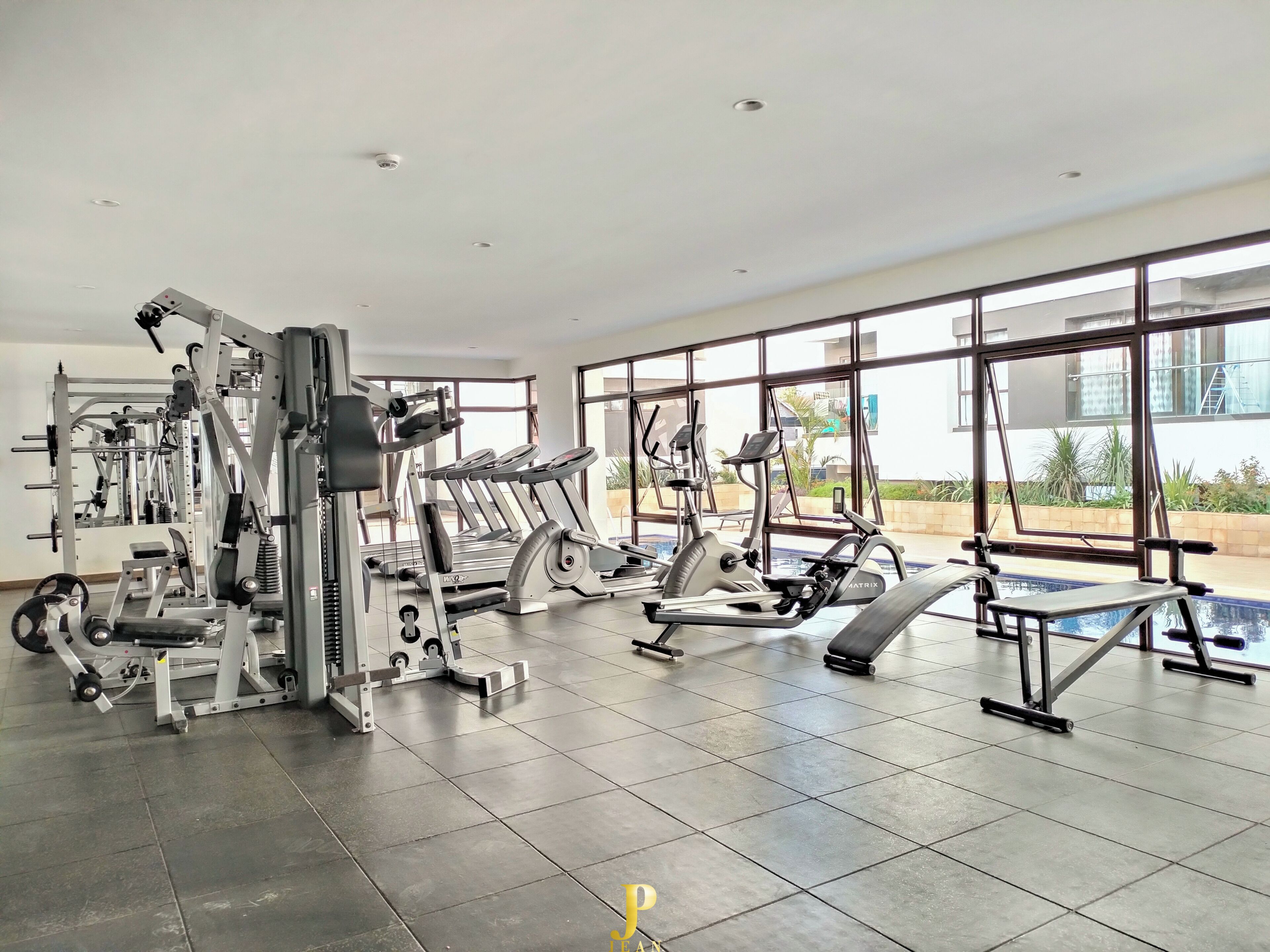 A gym with various exercise equipment, large windows, and a tiled floor.