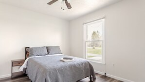 A bedroom with a large window, a bed with grey bedding, a nightstand, and a ceiling fan. - The place of possibilities with amazing heated pool. (Pulaski)