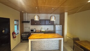 Une cuisine moderne avec des meubles en bois, un îlot central, des suspensions en acier inoxydable, un four à micro-ondes, une cuisinière à gaz et un réfrigérateur.