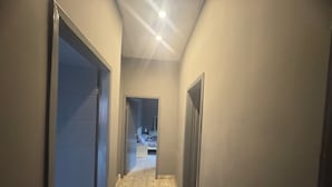 Un couloir étroit, dont le sol est recouvert de carreaux décoratifs, mène à une chambre à coucher équipée d’un lit et d’une table de chevet.