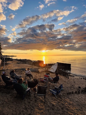 Une scène de plage avec des personnes assises sur des chaises, une jetée en bois et un coucher de soleil.