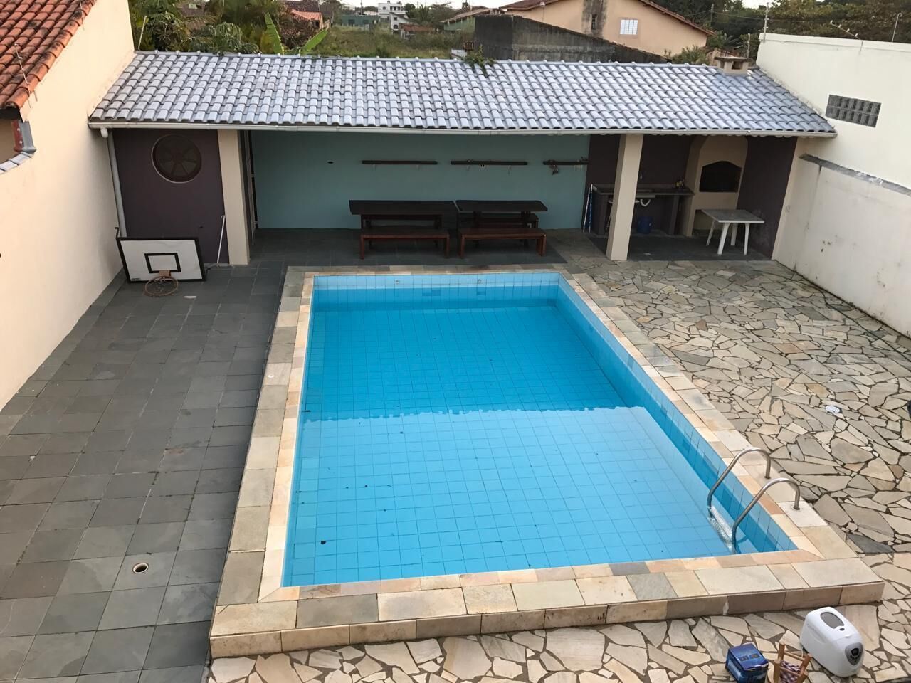A rectangular swimming pool with a tiled edge, surrounded by a stone patio.