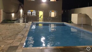 Ein Schwimmbecken mit einer Steindekke, ein zweigeschossiges Gebäude mit Rundbogenfenstern und eine Treppe, die zu der oberen Etage führt.