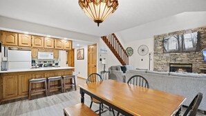 A spacious kitchen with wooden cabinets, a dining table with benches, a stone fireplace, and a staircase leading to another level.