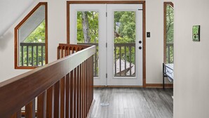 A hallway with a wooden railing, a double door with glass panels, and a bed with a white bedspread.