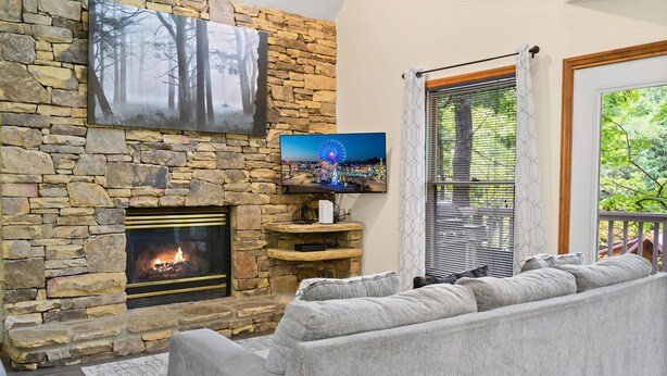 A stone fireplace with a TV mounted above it, a gray sofa, and a window with blinds.