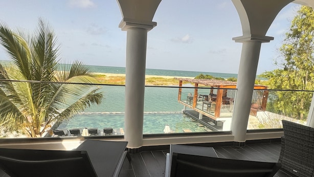 A balcony with two chairs, a pool, and a view of the beach and ocean. - La Parenthèse (Mbodiène)