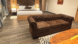 A modern bedroom with a large bed, a brown sofa, and a wooden coffee table. - La Parenthèse (Mbodiène)