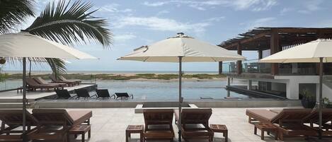 A poolside area with lounge chairs and umbrellas, overlooking a beach and ocean.