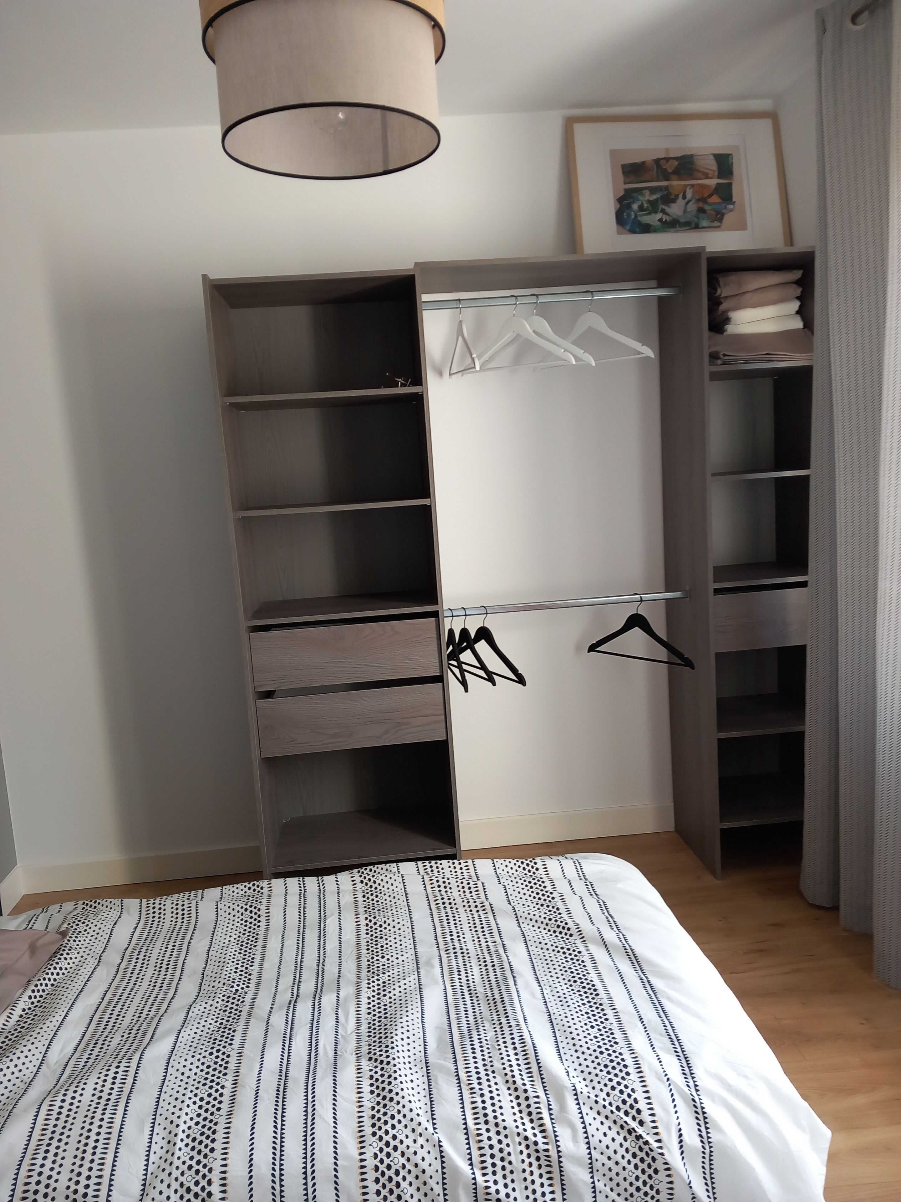 A bedroom with a bed, a wardrobe with multiple shelves, and a hanging area.
