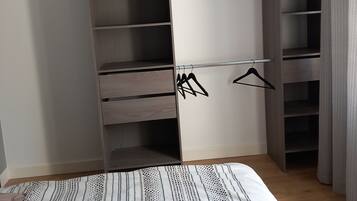 A bedroom with a bed, a wardrobe with multiple shelves, and a hanging area.