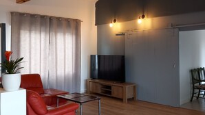 A living room with a red sofa, wooden flooring, a TV, and a ceiling with exposed beams.