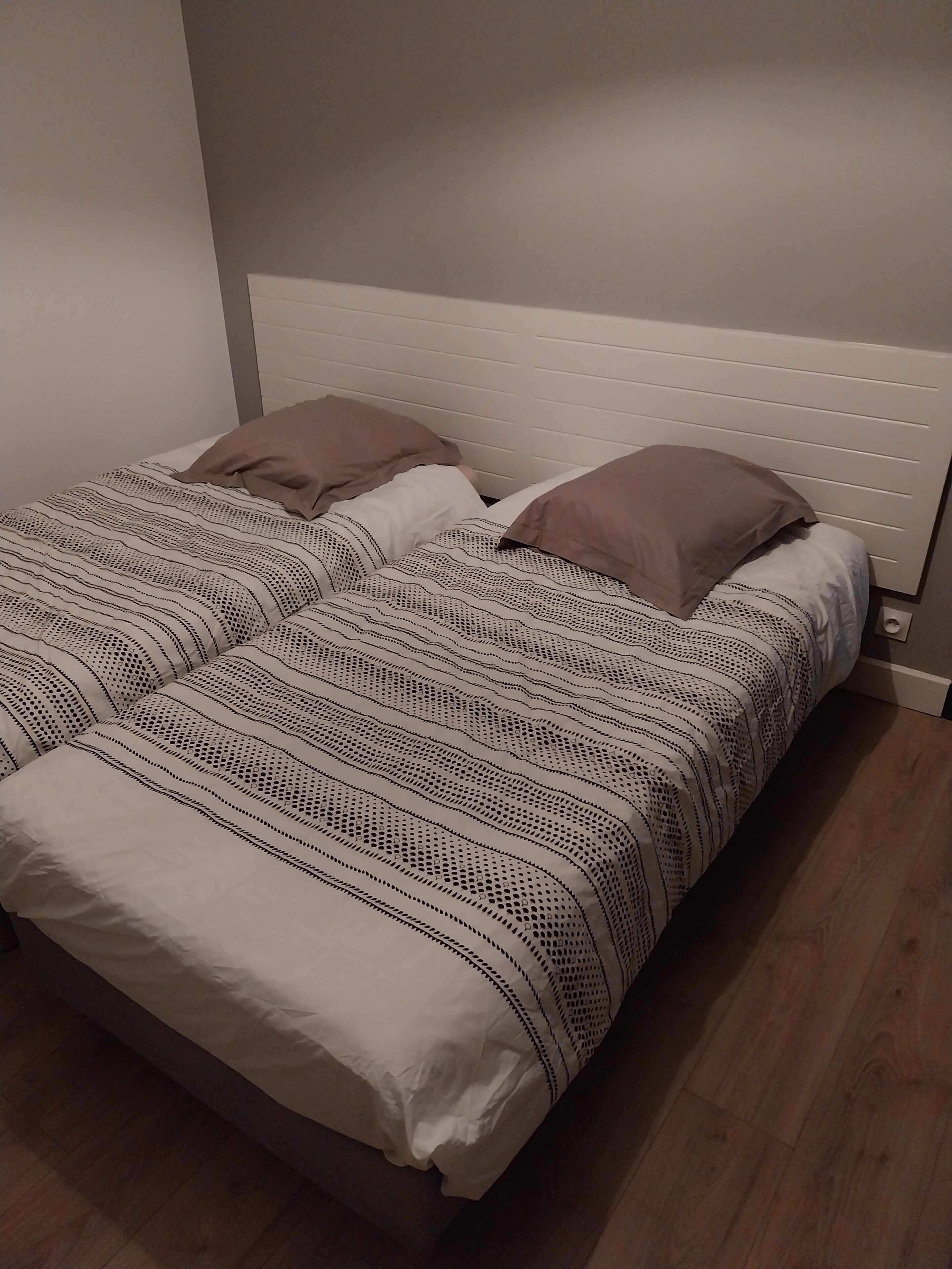 A double bed with a white headboard, two pillows, and a patterned bedspread.