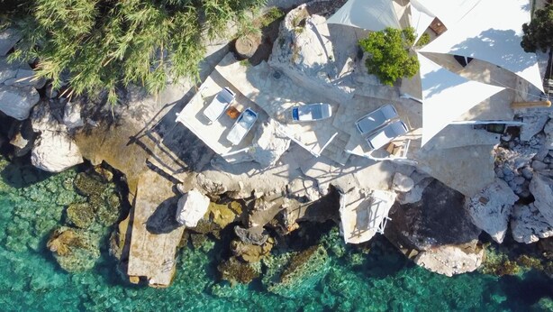 An aerial view of a coastal property with multiple white structures, some with lounge chairs, surrounded by clear turquoise waters and rocky terrain. - house for two with a private terrace located directly on the beach, town Hvar (Hvar)