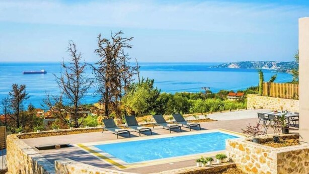 Un área de piscina con sillones reclinables, un muro de piedra y vista al mar.
