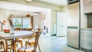 Una cocina moderna con un refrigerador de acero inoxidable, un comedor con una mesa redonda y sillas, y vistas al exterior a través de amplios ventanales.