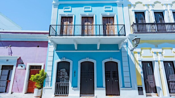 Un edificio de varios pisos con balcón, puertas grandes y un letrero sobre la entrada.