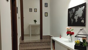 Ein Flur mit weißer Wand, einer Weltkarte im Rahmen, einem kleinen Tisch mit Pflanze und einer Treppe mit gemustertem Teppich.
