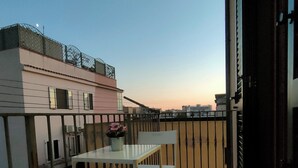 Ein Balkon mit Tisch und Stühlen, einem Blumentopf und Blick auf Gebäude im Hintergrund.