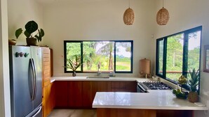 A modern kitchen with a refrigerator, stove, and large windows offering a view of greenery.