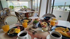 A breakfast setting with a table set for two, featuring plates of food, glasses of orange juice, and cups of coffee. - All Seasons Hotel Bayahibe (San Rafael del Yuma)
