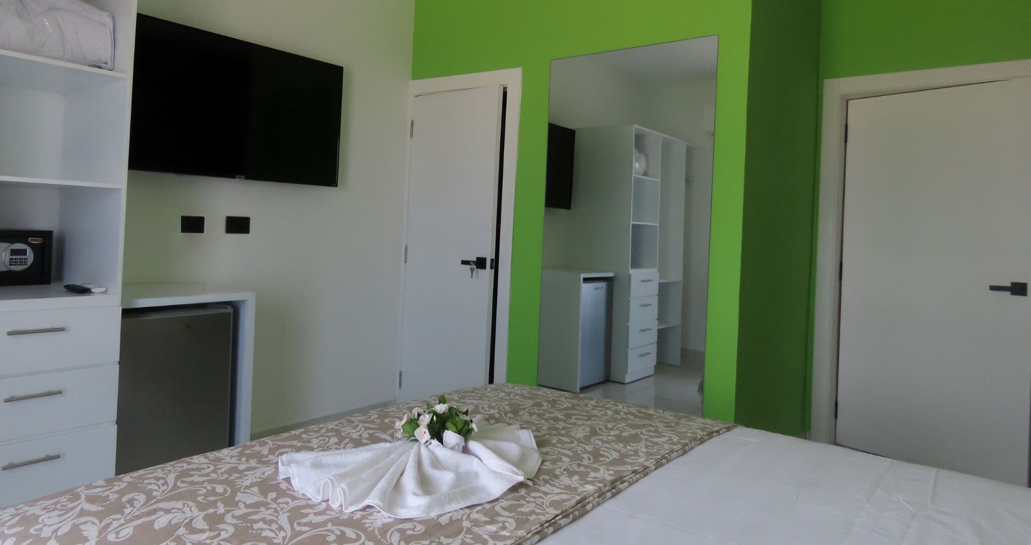 Ein Hotelzimmer mit Bett, Schreibtisch mit Computer, Kleiderschrank und Wandfernseher.