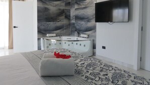 A modern bathroom with a glass-enclosed bathtub, a flat-screen TV mounted on the wall, and a patterned floor. - All Seasons Hotel Bayahibe (San Rafael del Yuma)