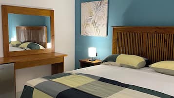 Une chambre à coucher avec une tête de lit en bois, un lit recouvert d’une courtepointe, une table de chevet avec une lampe, un miroir et un ventilateur de plafond.