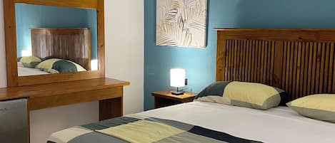 A bedroom with a wooden headboard, a bed with a quilt, a nightstand with a lamp, a mirror, and a ceiling fan.