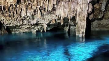 Une grotte ornée de stalactites et de stalagmites, avec une eau d’un bleu cristallin et un plafond rocheux.
