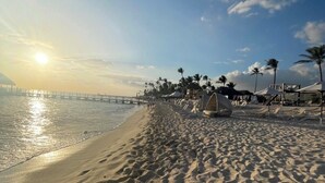 A beach with a pier extending into the water, palm trees, and beach umbrellas. - All Seasons Hotel Bayahibe (San Rafael del Yuma)