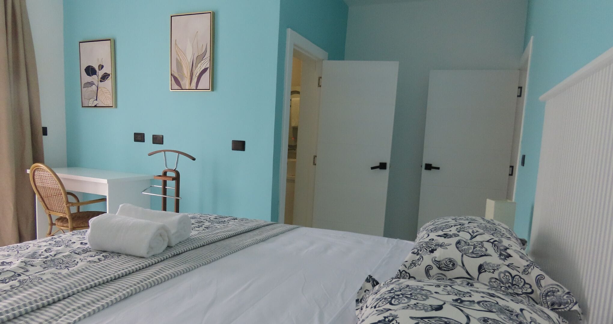 A bedroom with a bed, a desk, and a chair. There are two doors leading to other rooms.