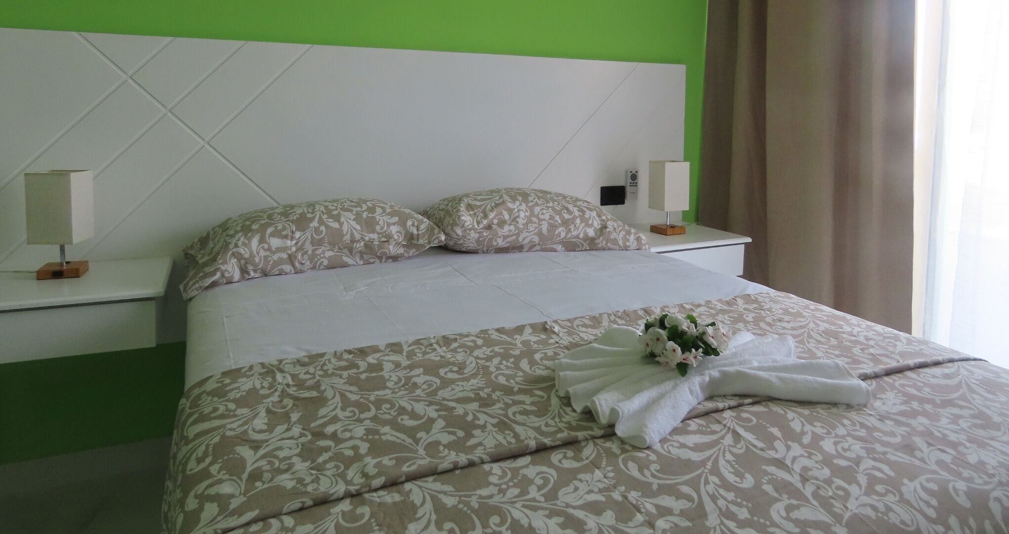 A hotel room with a large bed, two bedside tables, a nightstand, and a green accent wall.