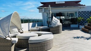 A rooftop terrace with wicker lounge chairs, a covered seating area, and a view of the cityscape. - All Seasons Hotel Bayahibe (San Rafael del Yuma)