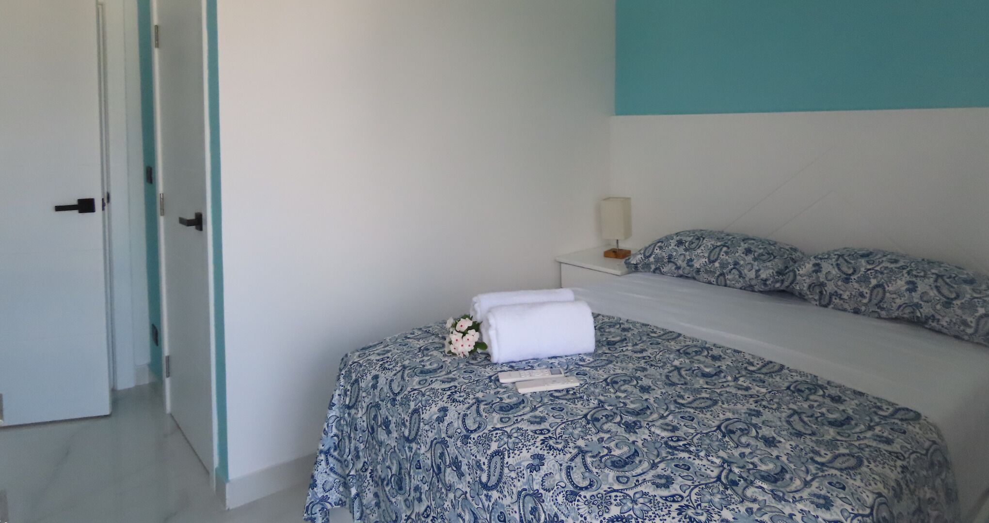 A bedroom with a bed, a nightstand, a lamp, and a door.