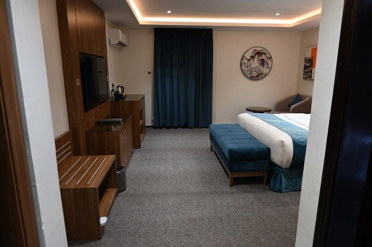 A hotel room with a bed, a desk, a chair, a TV, and a curtain.