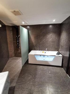 A modern bathroom with a freestanding bathtub, dark marble walls, and a light-colored floor.