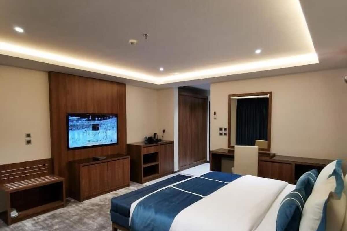 A modern hotel room with a large bed, a TV mounted on the wall, a desk, and a seating area.