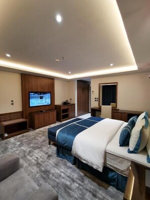 A modern hotel room with a large bed, a TV mounted on the wall, a desk, and a seating area.