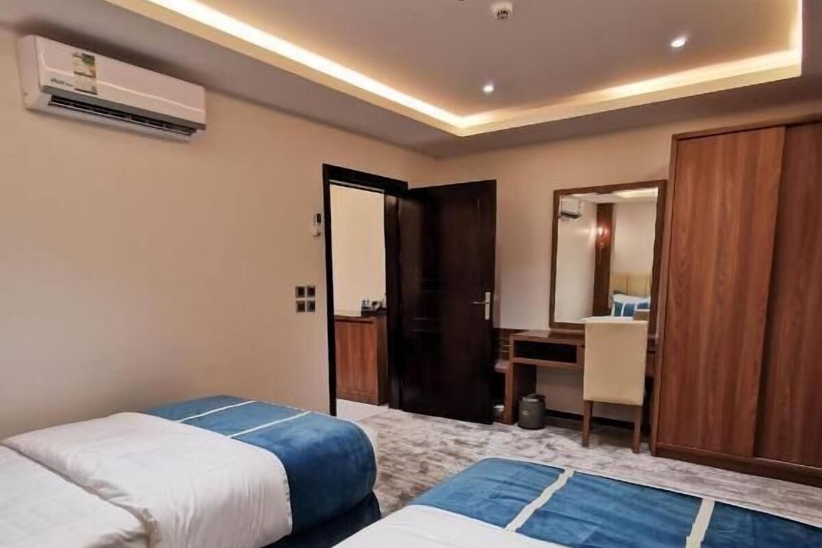 A hotel room with two beds, a desk, a chair, a mirror, and an air conditioning unit.