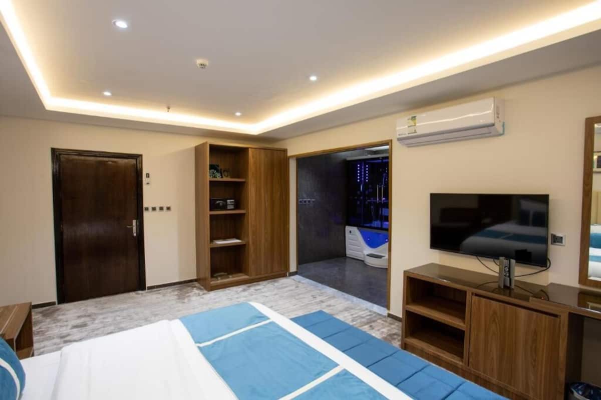 A modern hotel room with a bed, a TV, a wardrobe, and a bathroom visible through an open door.