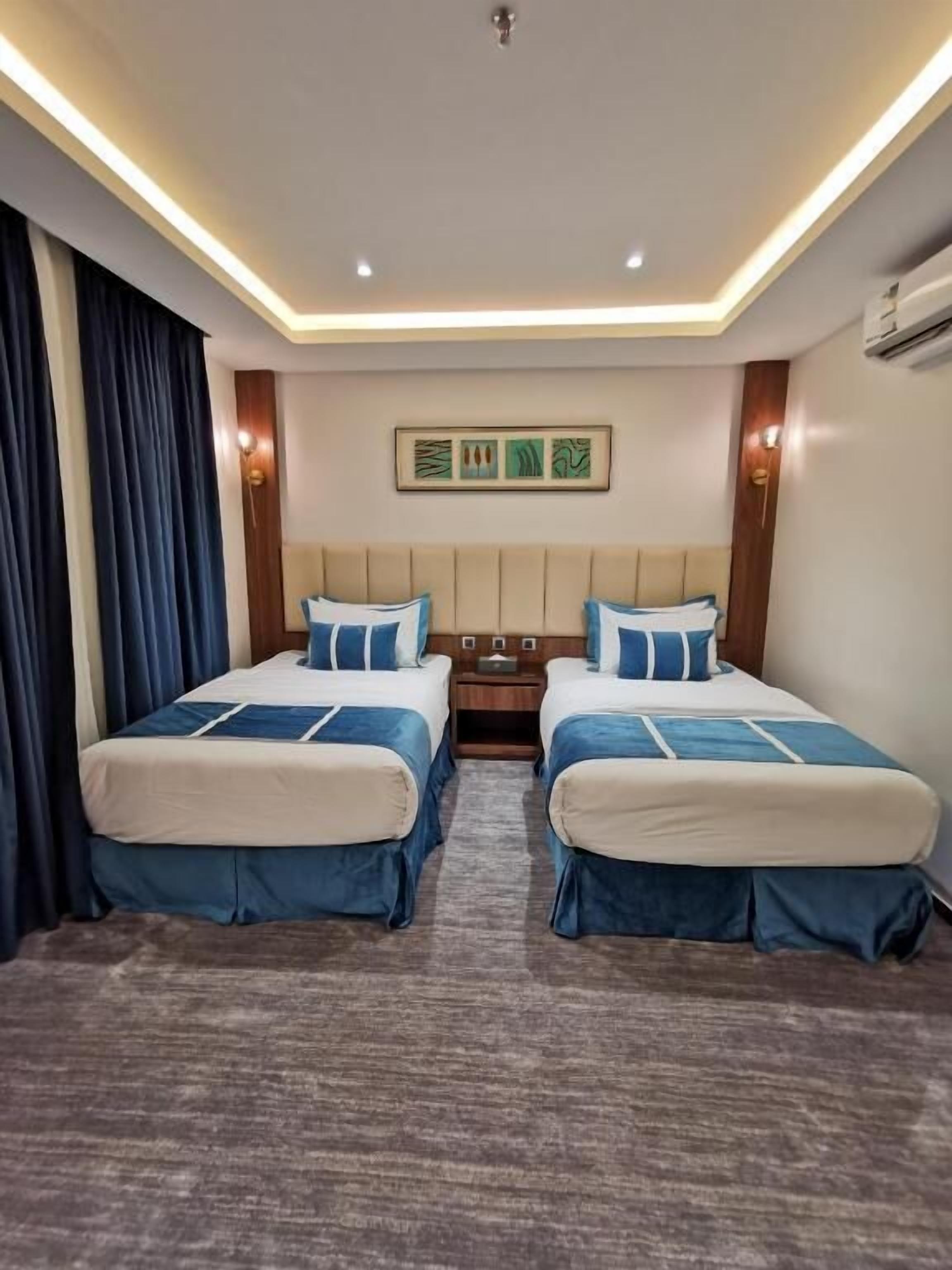 A hotel room with two beds, a nightstand, a ceiling light, and a wall-mounted air conditioner.