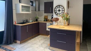 A modern kitchen with dark cabinets, a central island, and a large wall clock. - House for 6 people ideally located, close to many leisure activities (La Chapelle-Huon)