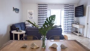 A dining area with a wooden table, a vase with a plant, and rocks. There is a blue sofa and a small round table with a vase and a book in the background. - Stay a While - 3 min walk to private beach access!

 (Destin)